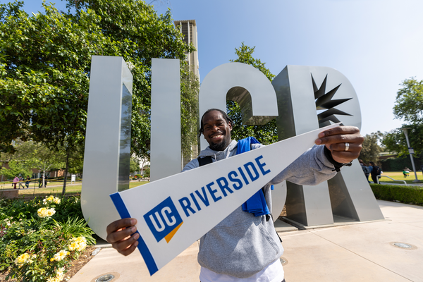 A student stands in front of the campus UCR letters holding a UC Riverside pennant flag